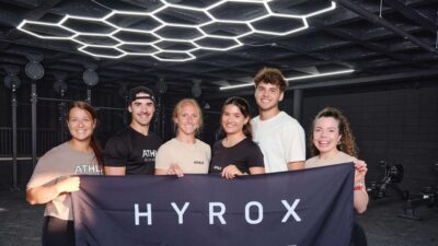 Une photo des propriétaires du nouveau gym ATHLX tenant une bannière HYROX.